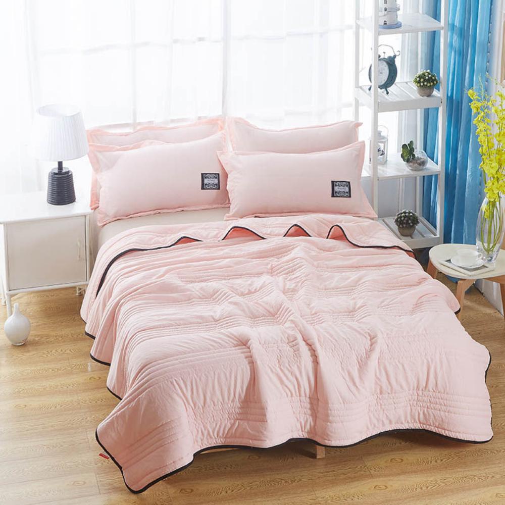 The cooling blanket in light pink on a bed in a bedroom.